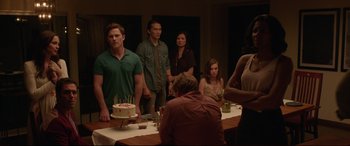 Movie still from “The Invitation” (2015), directed by Karyn Kusama – A group of people standing around a table with a cake on it; Medium shot, Over the shoulder angle