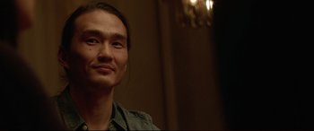 Movie still from “The Invitation” (2015), directed by Karyn Kusama – A man with long black hair is smiling for the camera; Close Up shot, Over the shoulder angle