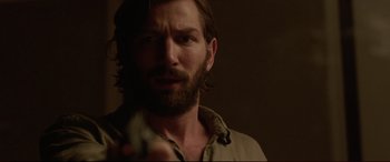 Movie still from “The Invitation” (2015), directed by Karyn Kusama – A man with long hair and a beard is holding a gun; Close Up shot, Over the shoulder angle