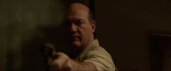 Movie still from “The Invitation” (2015), directed by Karyn Kusama – A bald man holding a gun in a room; Close Up shot, Over the shoulder angle