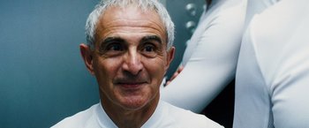 Movie still from “The Island” (2005), directed by Michael Bay – An older man wearing a white shirt and white jacket; Close Up shot, Low angle