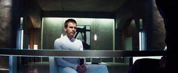 Movie still from “The Island” (2005), directed by Michael Bay – A man sitting on a chair holding a cell phone; Medium shot, Low angle