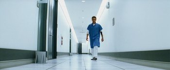 Movie still from “The Island” (2005), directed by Michael Bay – A man walking down a hall way wearing a blue lab coat; Wide shot, Low angle