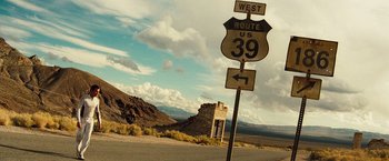 Movie still from “The Island” (2005), directed by Michael Bay – A road sign on the side of the road near a building; Extreme Wide shot, Low angle