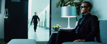 Movie still from “The Island” (2005), directed by Michael Bay – A man walking down a hallway in front of a man in a black suit; Wide shot, Over the shoulder angle