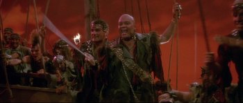 Movie still from “The Jewel of the Nile” (1985), directed by Lewis Teague – A couple of men standing next to each other on top of a boat; Medium shot, High angle