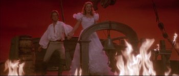Movie still from “The Jewel of the Nile” (1985), directed by Lewis Teague – A man and a woman dressed in white and standing next to a bell; Wide shot, Low angle