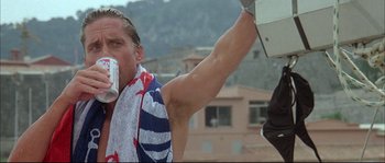 Movie still from “The Jewel of the Nile” (1985), directed by Lewis Teague – A man with a towel around his neck is drinking a beverage; Medium shot, Low angle