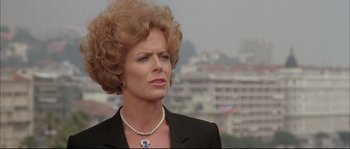 Movie still from “The Jewel of the Nile” (1985), directed by Lewis Teague – An older woman wearing a black suit and pearl necklace; Close Up shot, Low angle