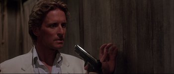 Movie still from “The Jewel of the Nile” (1985), directed by Lewis Teague – A man in a white jacket holding a gun; Close Up shot, Over the shoulder angle