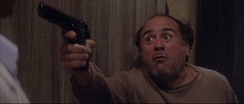 Movie still from “The Jewel of the Nile” (1985), directed by Lewis Teague – A man holding a gun up to his face; Medium shot, Low angle