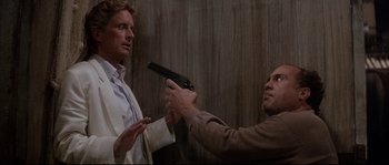 Movie still from “The Jewel of the Nile” (1985), directed by Lewis Teague – A man holding a gun pointed at another man in front of a wall; Medium shot, Over the shoulder angle