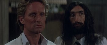 Movie still from “The Jewel of the Nile” (1985), directed by Lewis Teague – A man standing next to another man with long hair; Close Up shot, Over the shoulder angle