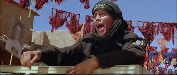Movie still from “The Jewel of the Nile” (1985), directed by Lewis Teague – A man in a black jacket and a black hat is crying; Medium shot, Low angle