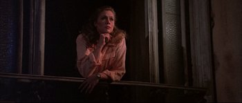 Movie still from “The Jewel of the Nile” (1985), directed by Lewis Teague – A woman leaning on a railing in front of a window; Medium shot, Low angle