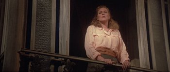 Movie still from “The Jewel of the Nile” (1985), directed by Lewis Teague – A woman standing on a balcony looking out of a window; Medium shot, Low angle