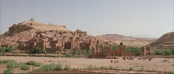 Movie still from “The Jewel of the Nile” (1985), directed by Lewis Teague – People are standing in the dirt near a large city; Extreme Wide shot, High angle