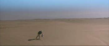 A man is running through the desert with a frisbee