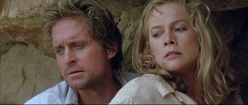 Movie still from “The Jewel of the Nile” (1985), directed by Lewis Teague – A man and a woman sitting next to each other in front of a stone wall; Close Up shot, Low angle