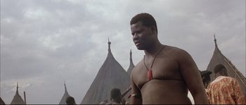 Movie still from “The Jewel of the Nile” (1985), directed by Lewis Teague – A man standing in front of a group of tents; Close Up shot, Low angle