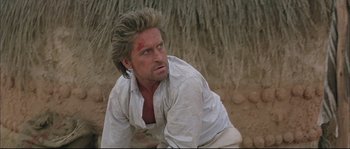 Movie still from “The Jewel of the Nile” (1985), directed by Lewis Teague – A person crouching on the ground; Close Up shot, Over the shoulder angle