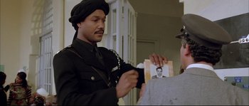 Movie still from “The Jewel of the Nile” (1985), directed by Lewis Teague – A man holding a picture of a man in a military uniform; Medium shot, Over the shoulder angle