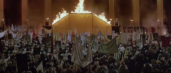 Movie still from “The Jewel of the Nile” (1985), directed by Lewis Teague – A crowd of people standing in front of a fire; Extreme Wide shot, High angle