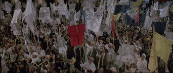 Movie still from “The Jewel of the Nile” (1985), directed by Lewis Teague – A large group of people are holding flags and banners; Wide shot, High angle