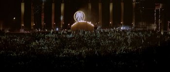 Movie still from “The Jewel of the Nile” (1985), directed by Lewis Teague – A crowd of people standing in front of a stage at night; Extreme Wide shot, High angle