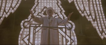 Movie still from “The Jewel of the Nile” (1985), directed by Lewis Teague – A man standing in front of a building with lights on it; Wide shot, Low angle