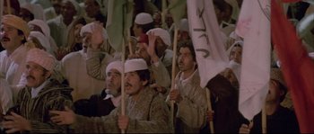 Movie still from “The Jewel of the Nile” (1985), directed by Lewis Teague – A group of men holding white flags in front of a crowd of onlookers; Medium shot, High angle