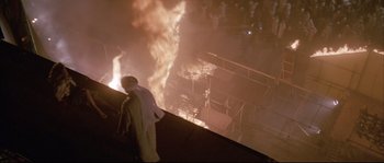 Movie still from “The Jewel of the Nile” (1985), directed by Lewis Teague – A man standing in front of a burning building at night; Extreme Wide shot, High angle