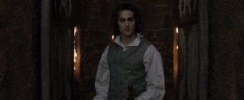 Movie still from “Queen of the Damned” (2002), directed by Michael Rymer – A man in a vest holding a sword in front of a brick wall; Medium shot, Over the shoulder angle