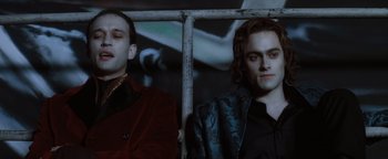 Movie still from “Queen of the Damned” (2002), directed by Michael Rymer – Two men sitting next to each other in front of a metal fence; Medium shot, Low angle