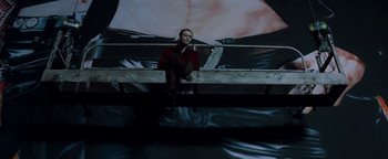 Movie still from “Queen of the Damned” (2002), directed by Michael Rymer – A man sitting on top of a railing in front of a painting; Wide shot, Low angle