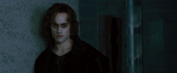Movie still from “Queen of the Damned” (2002), directed by Michael Rymer – A young man in a black shirt is standing in a dark room; Medium shot, Over the shoulder angle