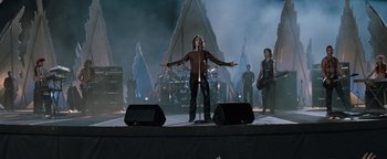 Movie still from “Queen of the Damned” (2002), directed by Michael Rymer – A man standing on a stage holding a microphone; Wide shot, Low angle