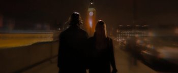 Two people standing on the side of a bridge at night