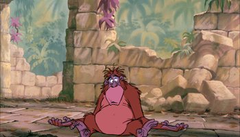 Movie still from “The Jungle Book” (1967), directed by Wolfgang Reitherman – A monkey sitting on the ground in front of a stone wall; Wide shot, Low angle