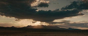 Movie still from “The Kid” (2019), directed by Vincent D'Onofrio – The sun is setting over a mountain range with dark clouds; Extreme Wide shot, Low angle