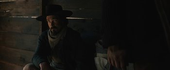 Movie still from “The Kid” (2019), directed by Vincent D'Onofrio – A man with a beard and a cowboy hat is sitting next to another man; Medium shot, Over the shoulder angle
