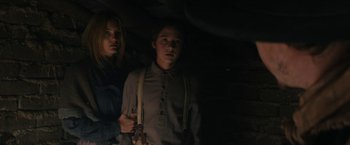 Movie still from “The Kid” (2019), directed by Vincent D'Onofrio – Two people standing in a dimly - lit room holding guns; Medium shot, Low angle