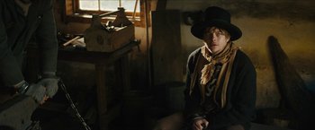 Movie still from “The Kid” (2019), directed by Vincent D'Onofrio – A man sitting in a room wearing a hat and a scarf; Medium shot, Low angle