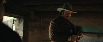Movie still from “The Kid” (2019), directed by Vincent D'Onofrio – A man wearing a hat and a coat standing next to a wall; Medium shot, Low angle