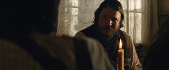 Movie still from “The Kid” (2019), directed by Vincent D'Onofrio – A man with long hair and a beard sitting in front of a window; Close Up shot, Over the shoulder angle