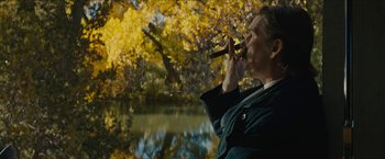 Movie still from “The Kid” (2019), directed by Vincent D'Onofrio – A man smoking a cigar near a body of water; Medium shot, Over the shoulder angle