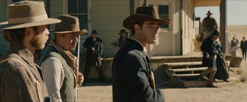 Movie still from “The Kid” (2019), directed by Vincent D'Onofrio – A man in a suit and a cowboy hat standing in front of other men; Medium shot, Over the shoulder angle