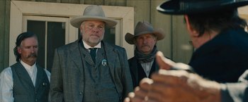 Movie still from “The Kid” (2019), directed by Vincent D'Onofrio – Two men in suits and hats standing next to each other in front of a building; Medium shot, Over the shoulder angle