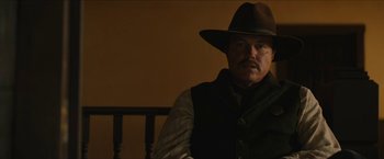 Movie still from “The Kid” (2019), directed by Vincent D'Onofrio – A man wearing a hat and vest sitting in front of a wooden chair; Close Up shot, Low angle