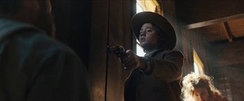 Movie still from “The Kid” (2019), directed by Vincent D'Onofrio – A man in a brown coat holding a gun in a room; Medium shot, Low angle